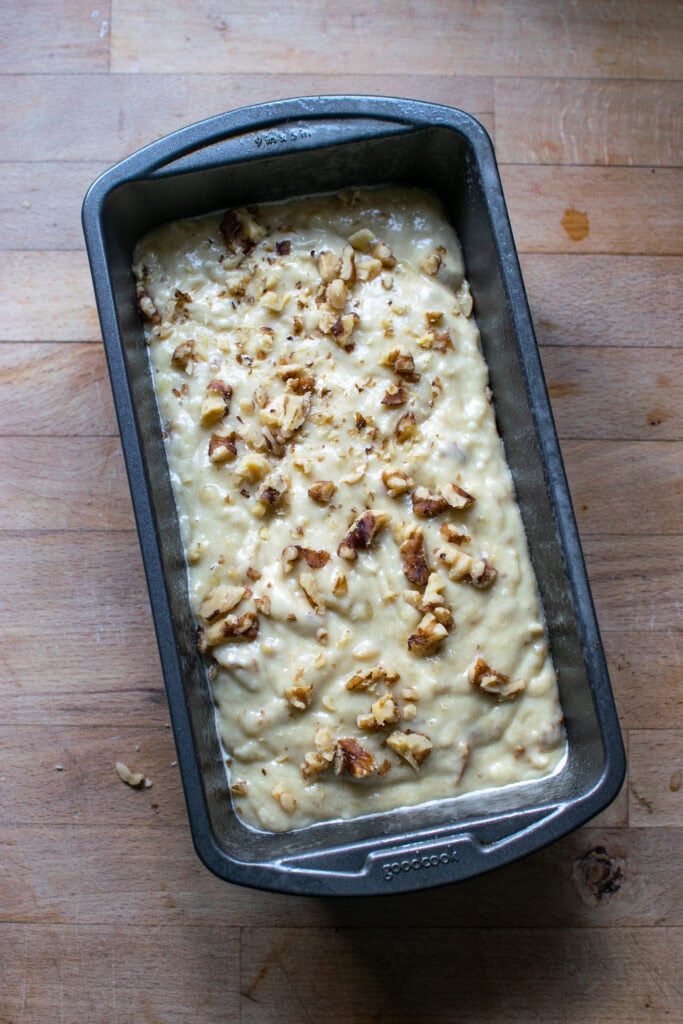 Banana bread bread batter poured into a loaf pan and topped with chopped walnuts.