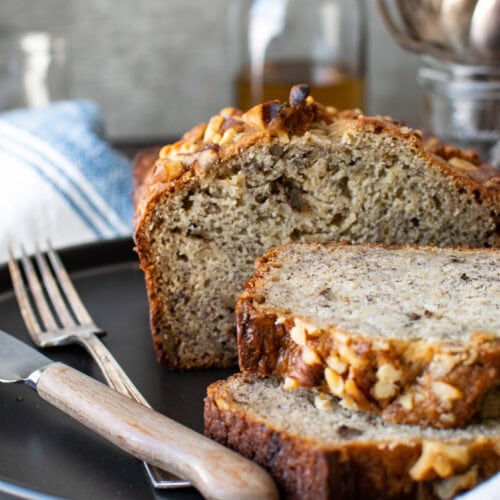 Banana rum bread on a black plate with two slices cut.