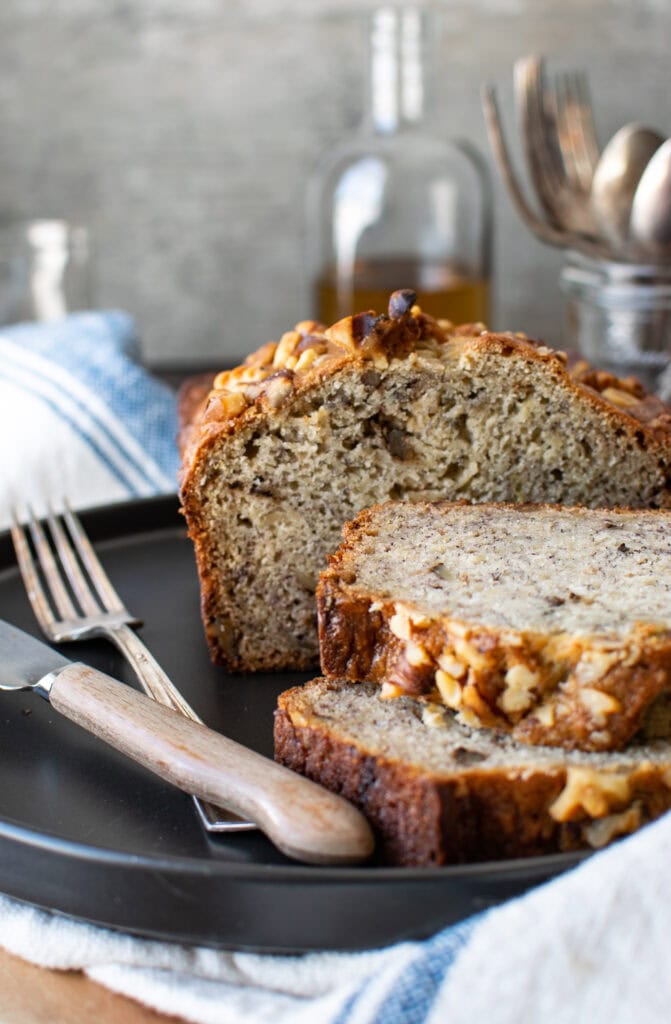 Banana rum bread on a black plate with two slices cut.