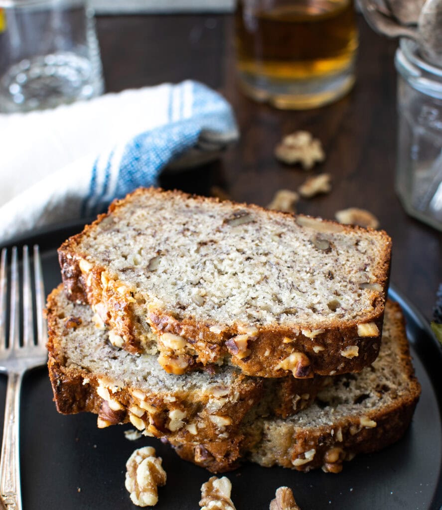 3 slices of banana bread stacked on a black plate.