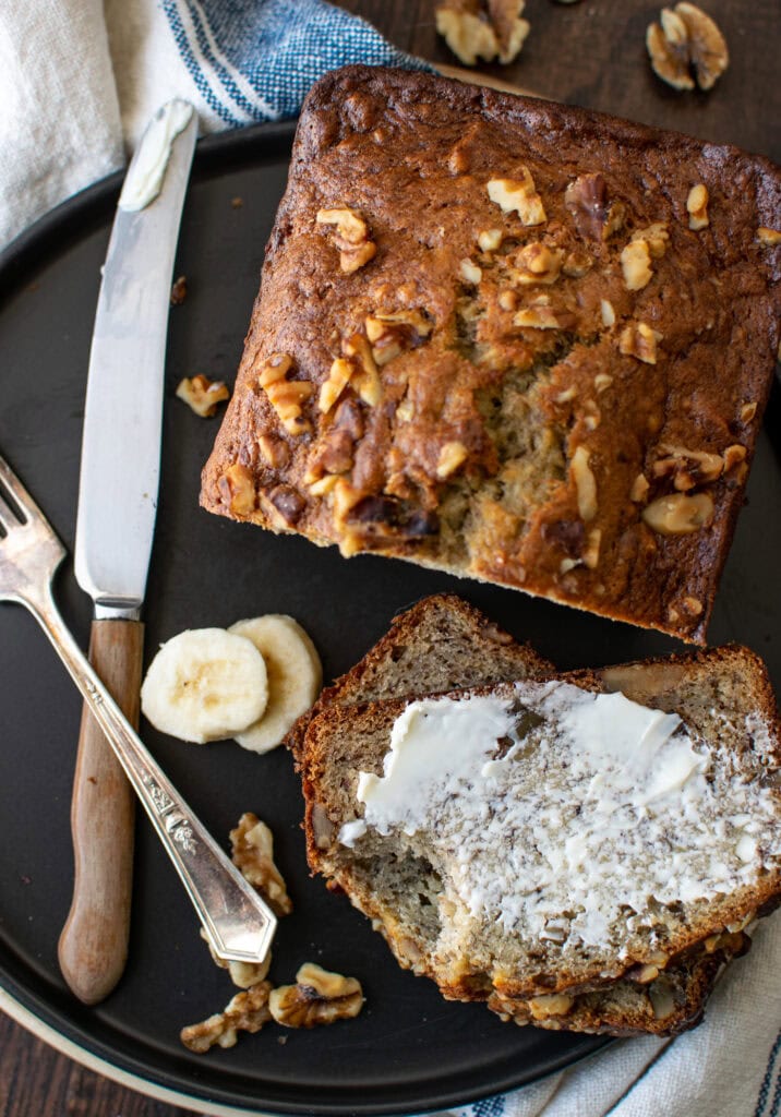 A loaf of banana rum bread with a slice that has been buttered.