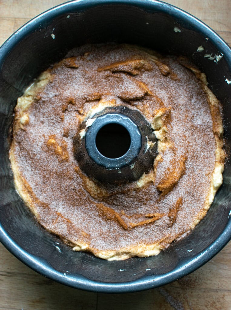 A bundt pan with half the cake batter, with a layer of sugar and cinnamon on top.