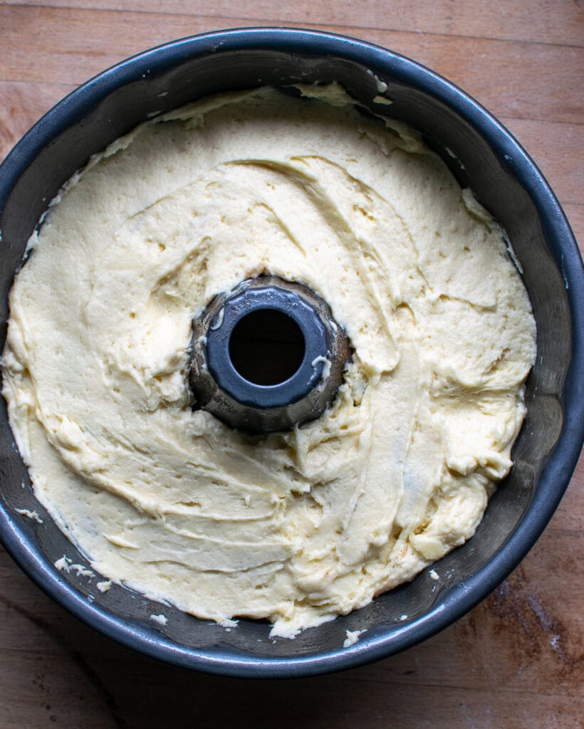 The second half of cake batter is spread over the cinnamon sugar and blueberries in a bundt pan.