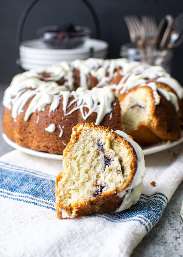 A blueberry sour cream coffee cake with a slice cut out and placed on a napkin.