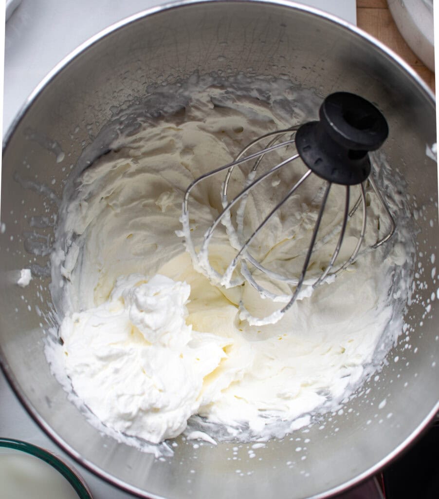 Freshly whipped cream in the bowl of an electric mixer with the whisk attachment.