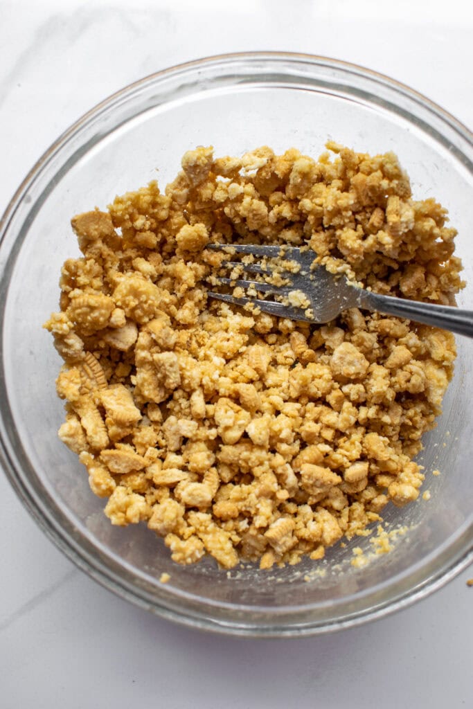 A glass bowl with a mixture of vanilla cookie crumbs and melted butter