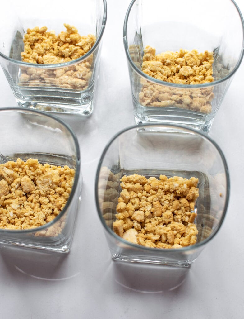 Dessert glasses with a layer of cookie crumb crust pressed into the bottom of each.