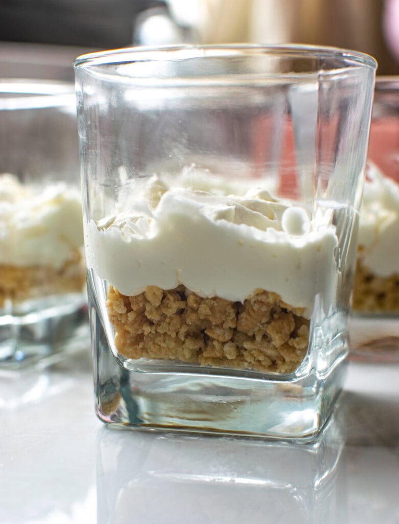 Glass dessert glasses with a layer of cookie crumbs topped with a layer of cream cheese.