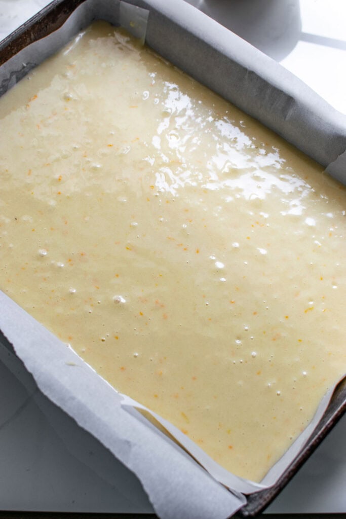 Cake batter in a 9 by 13 inch cake pan that is lined with parchment paper.