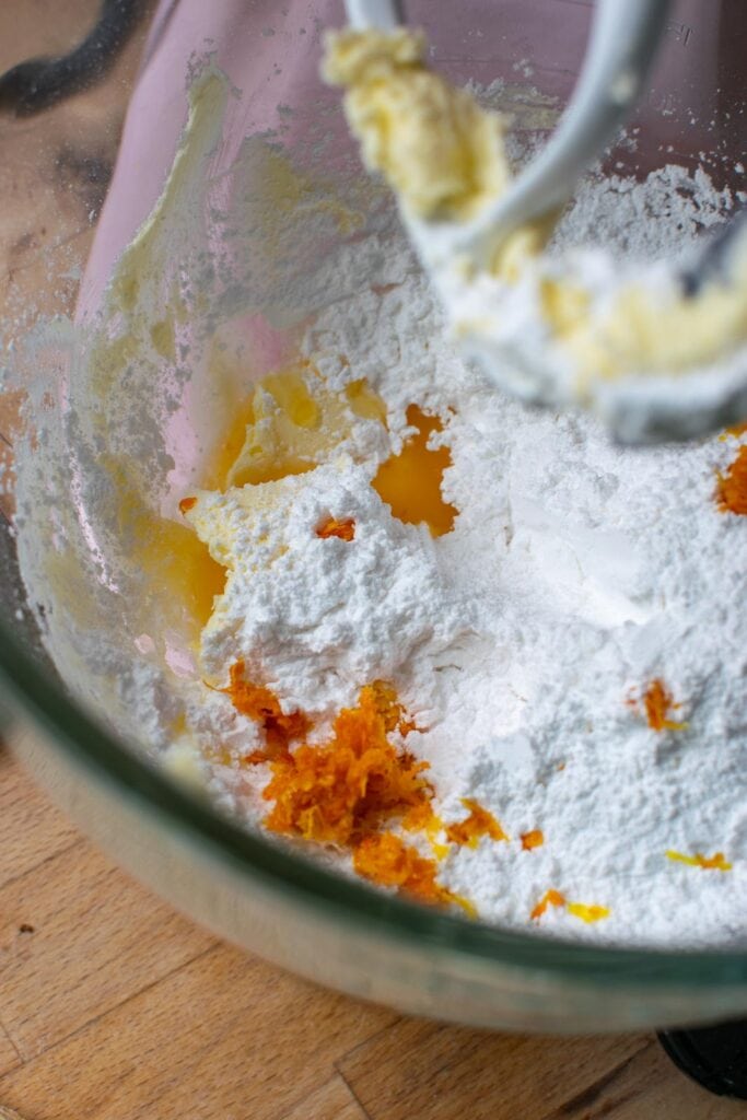 Ingredients to make orange flavoured buttercream frosting in the bowl of electric mixer.