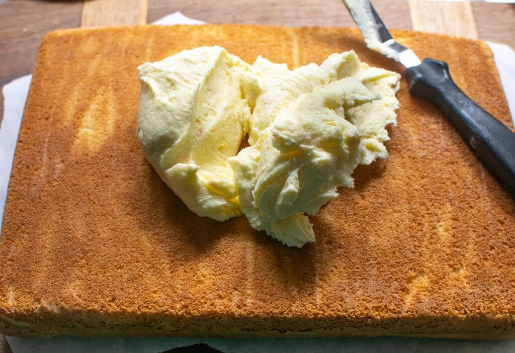 Orange buttercream frosting being spread onto a sheet cake.