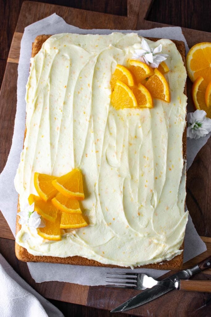 An orange sheet cake frosted with orange buttercream frosting and decorated in each corner with fresh orange slices cut into triangles.